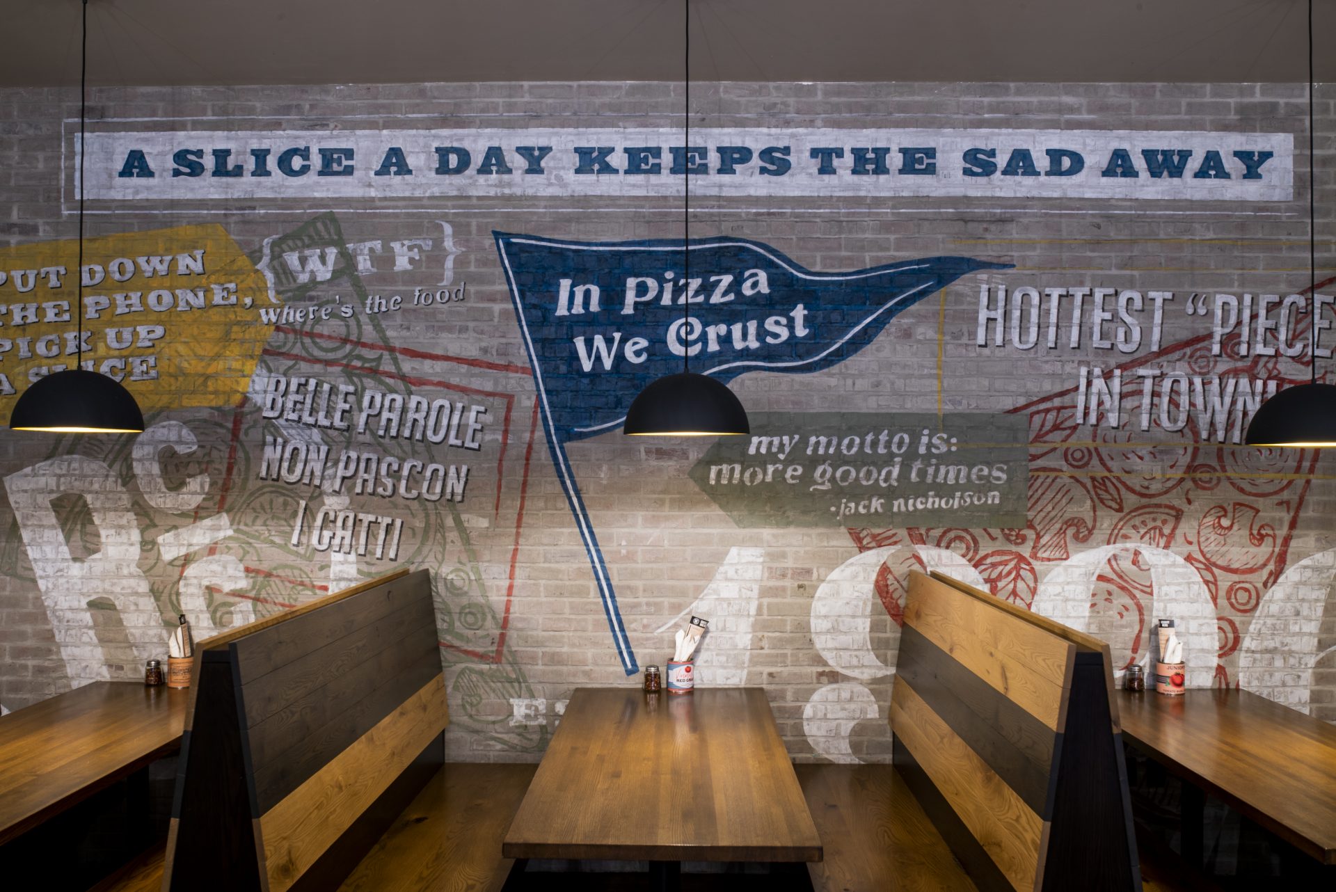 In Pizza We Trust painted on brick at booth seating